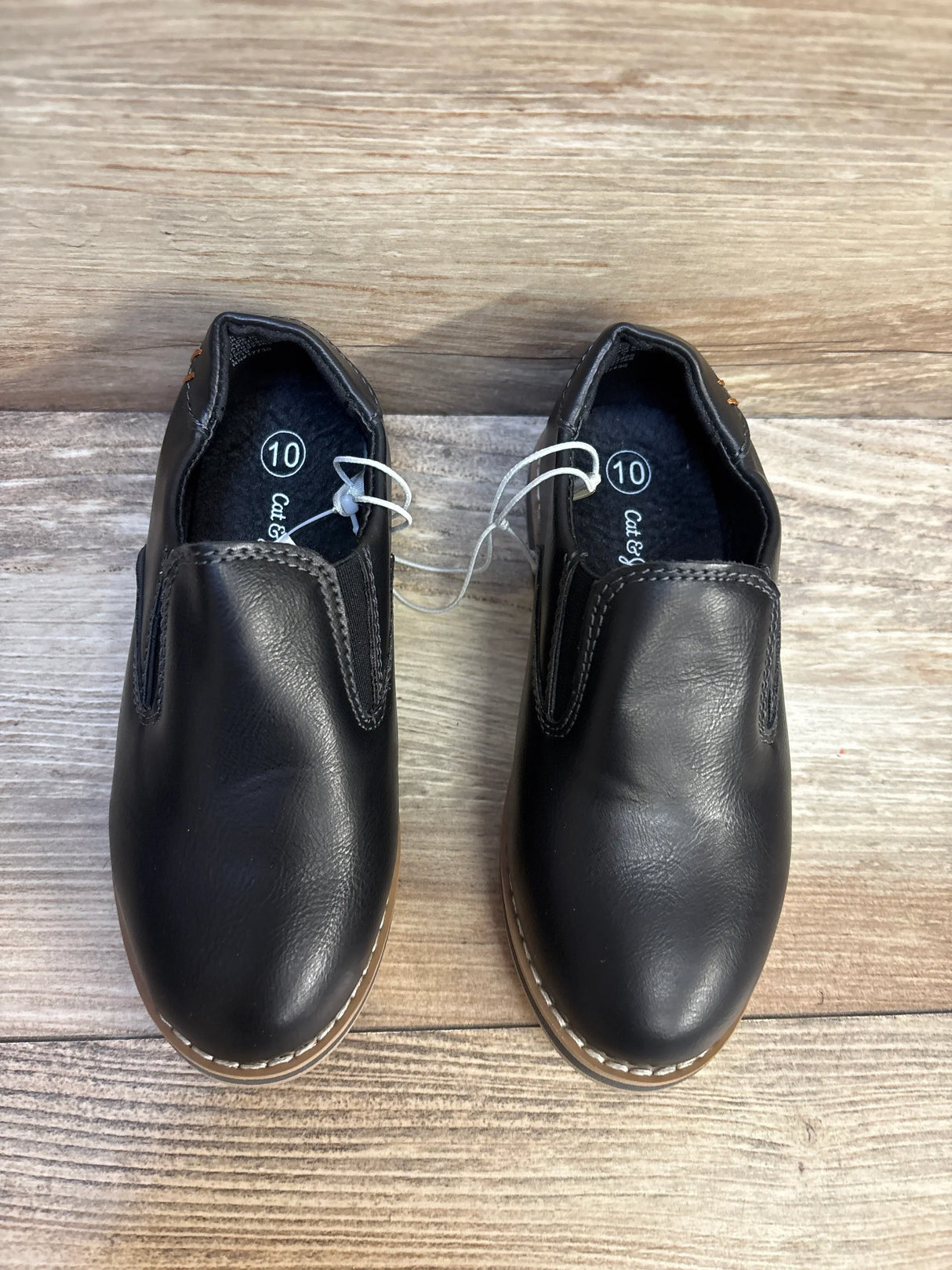 Black slip-on boys shoes size 10 with tan soles on wood background