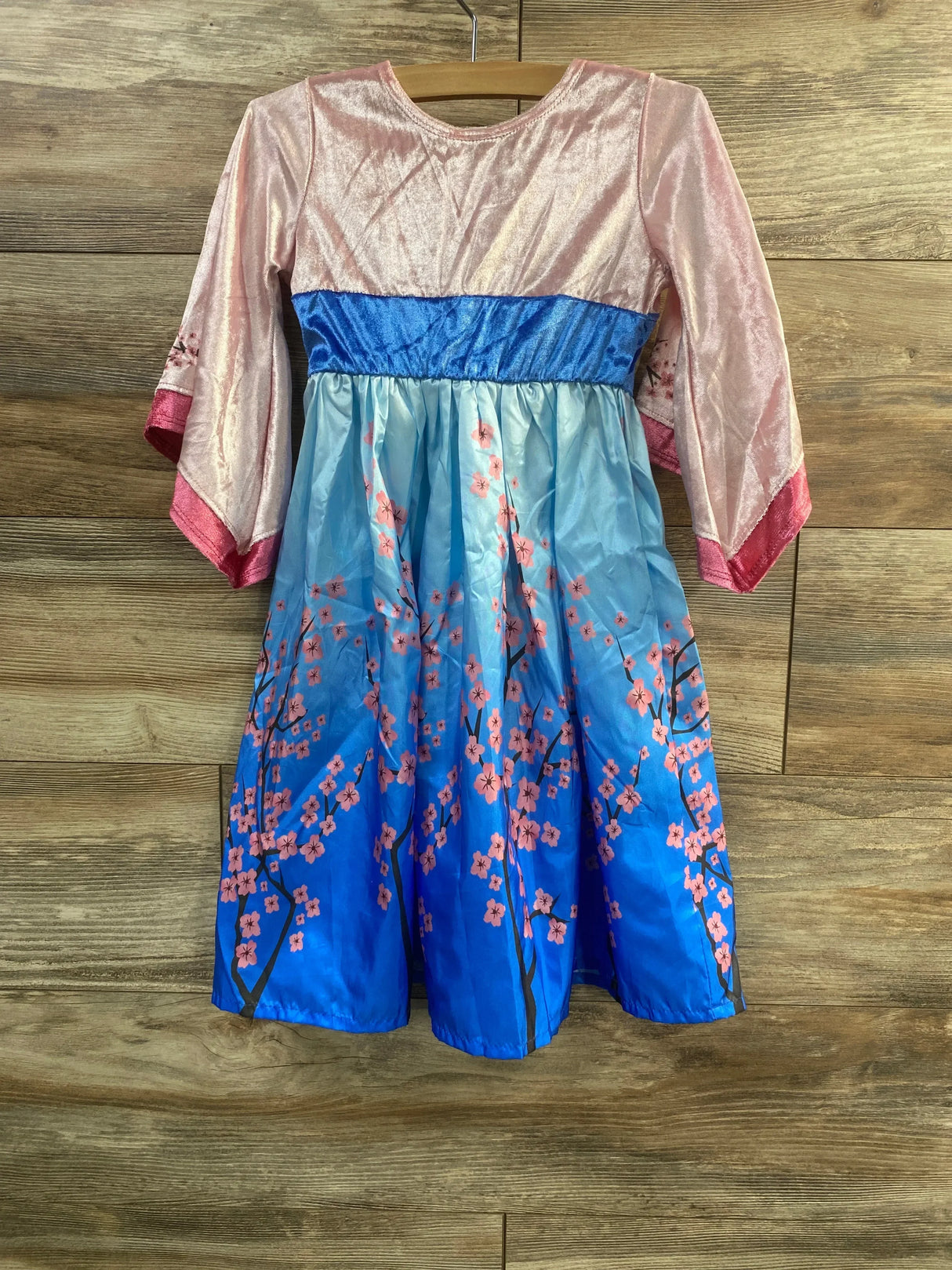 Front of cherry blossom twirl dress, 1-3Y, pink shimmer top, blue sash, ombre blue skirt with pink blossoms on wood background