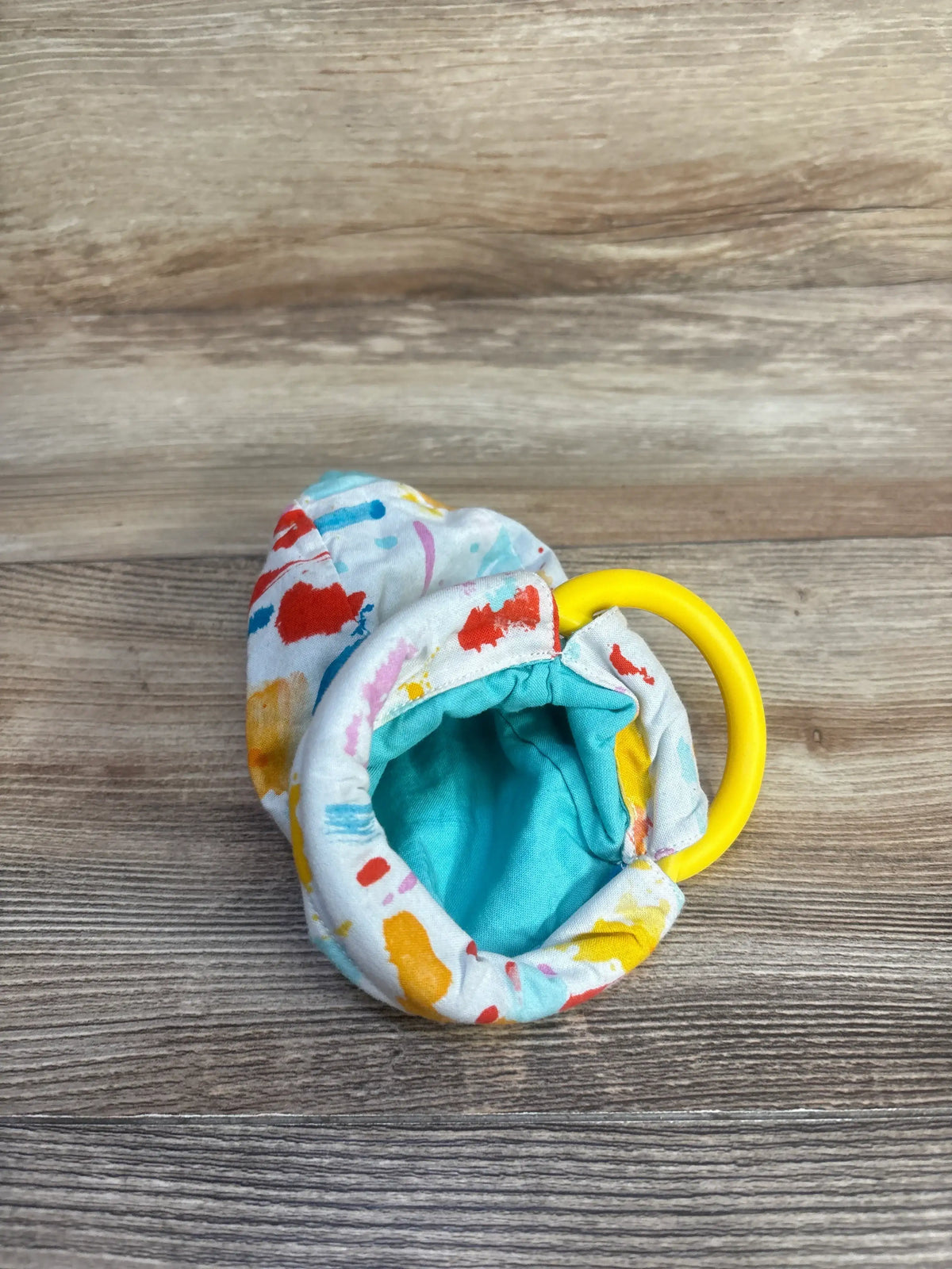 Top view of Lovevery Organic Cotton Sensory Pouch showcasing its open, colorful fabric and yellow ring on wood-grain background