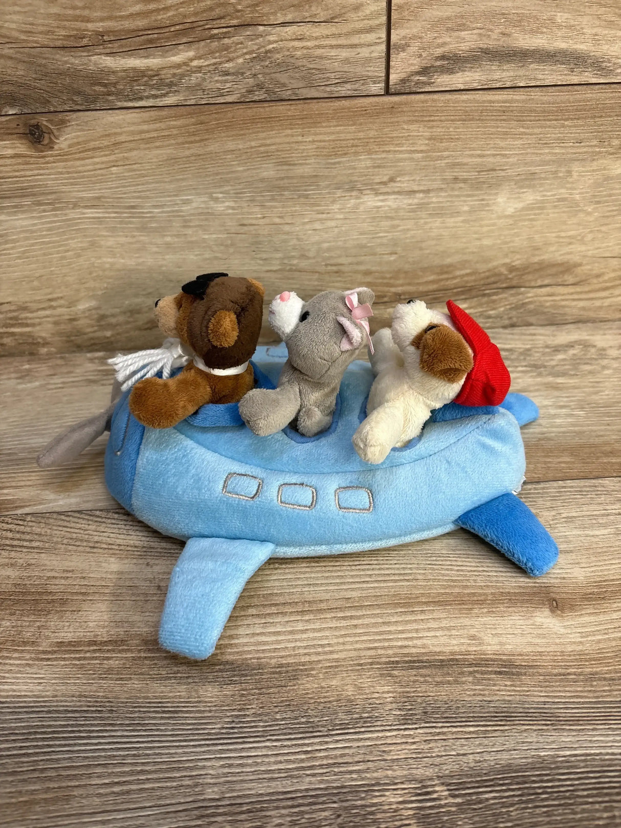 Front view of blue plush airplane with three puppets (bear, gray mouse with pink bow, dog with red hat) on wood background