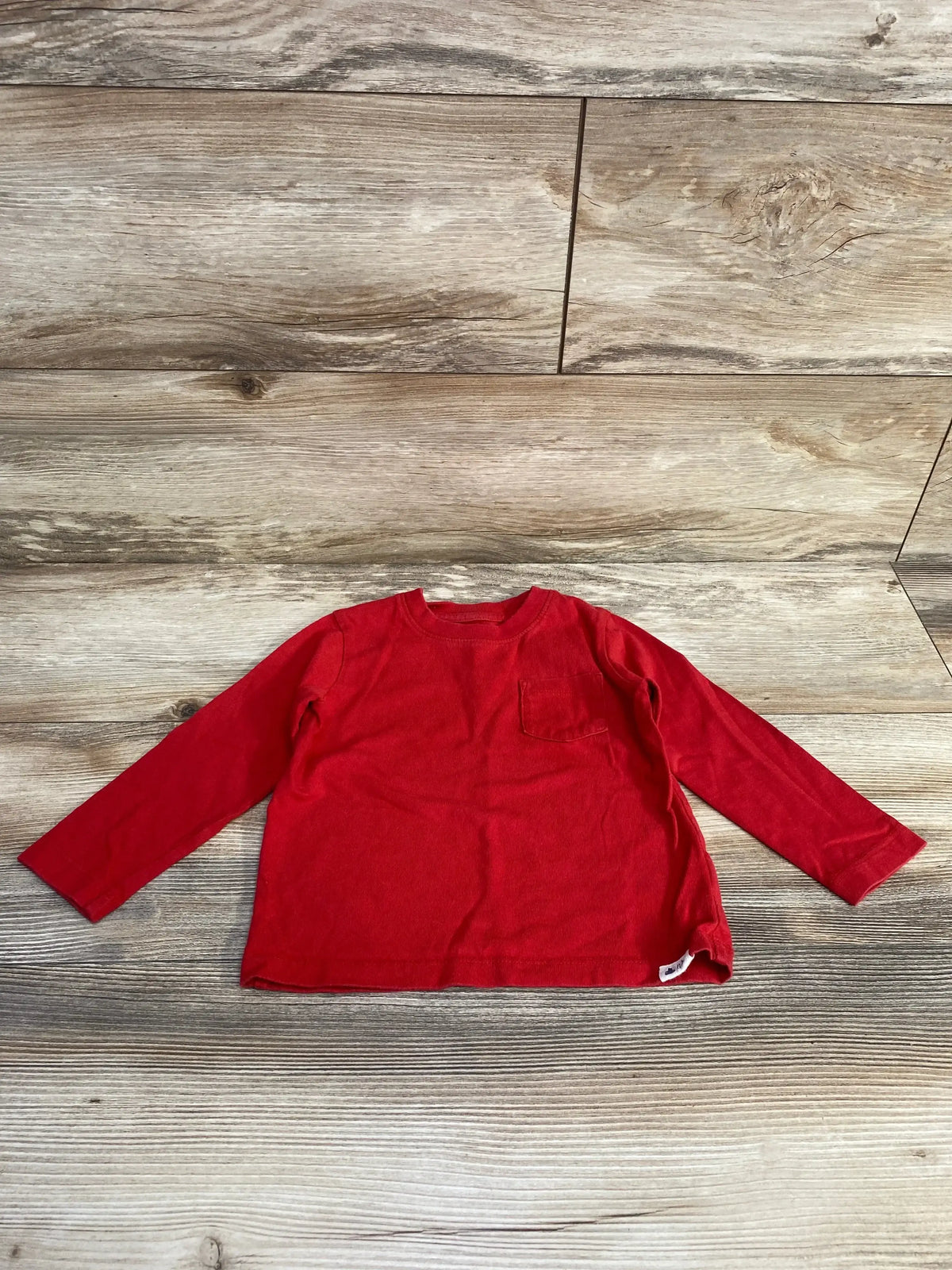Front view of Baby Gap red 100% cotton long-sleeve pocket shirt with crew neckline on wood plank background