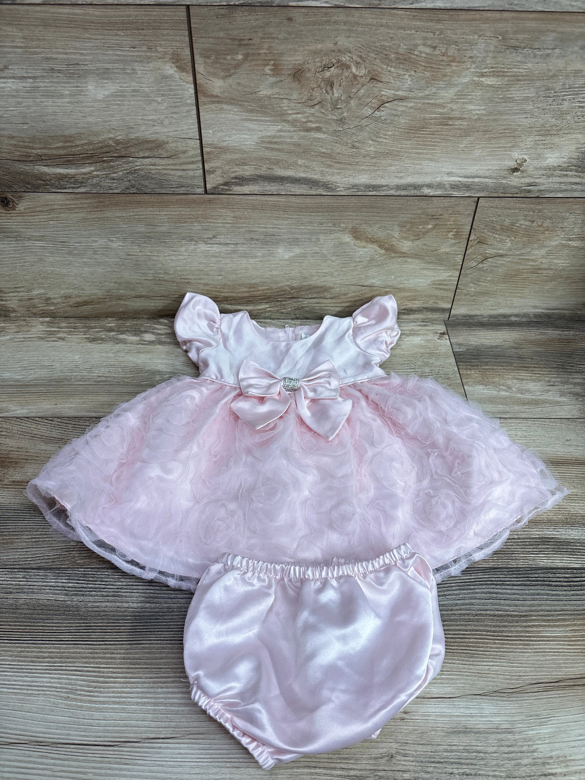 Top-down view of Rare Editions pink tulle dress and bloomers set showcasing satin bow and layered skirt on a wood floor