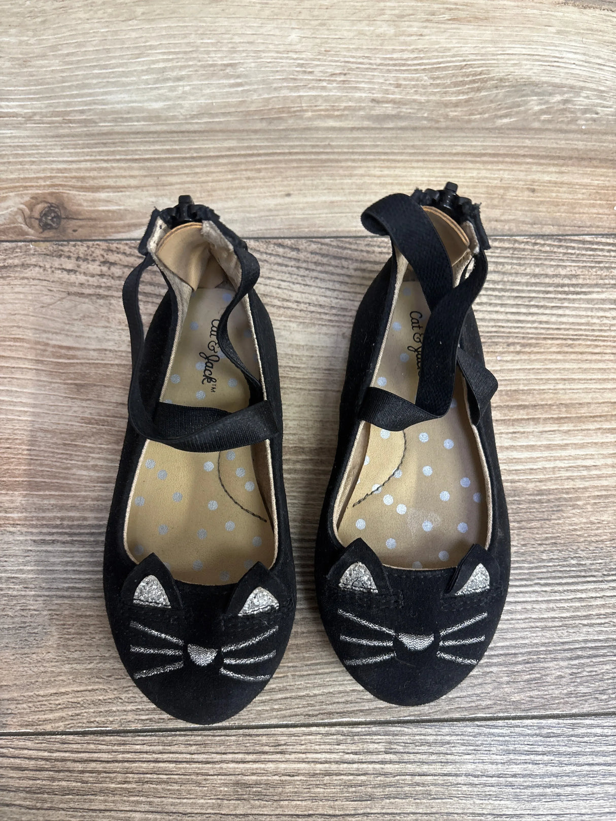 Black kids ballet flats with silver cat face and ears on wooden floor, children's shoes