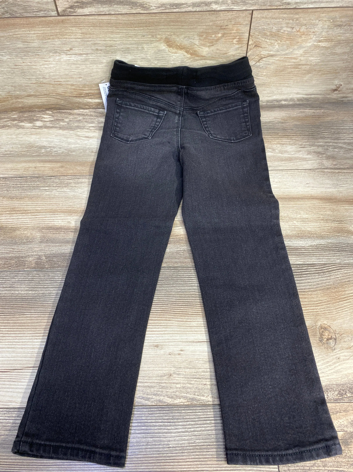 Back view of NWT Old Navy 360 Stretch rib-knit distressed skinny jeans sz 5T in black showcasing elastic waistband and pockets on wood plank floor