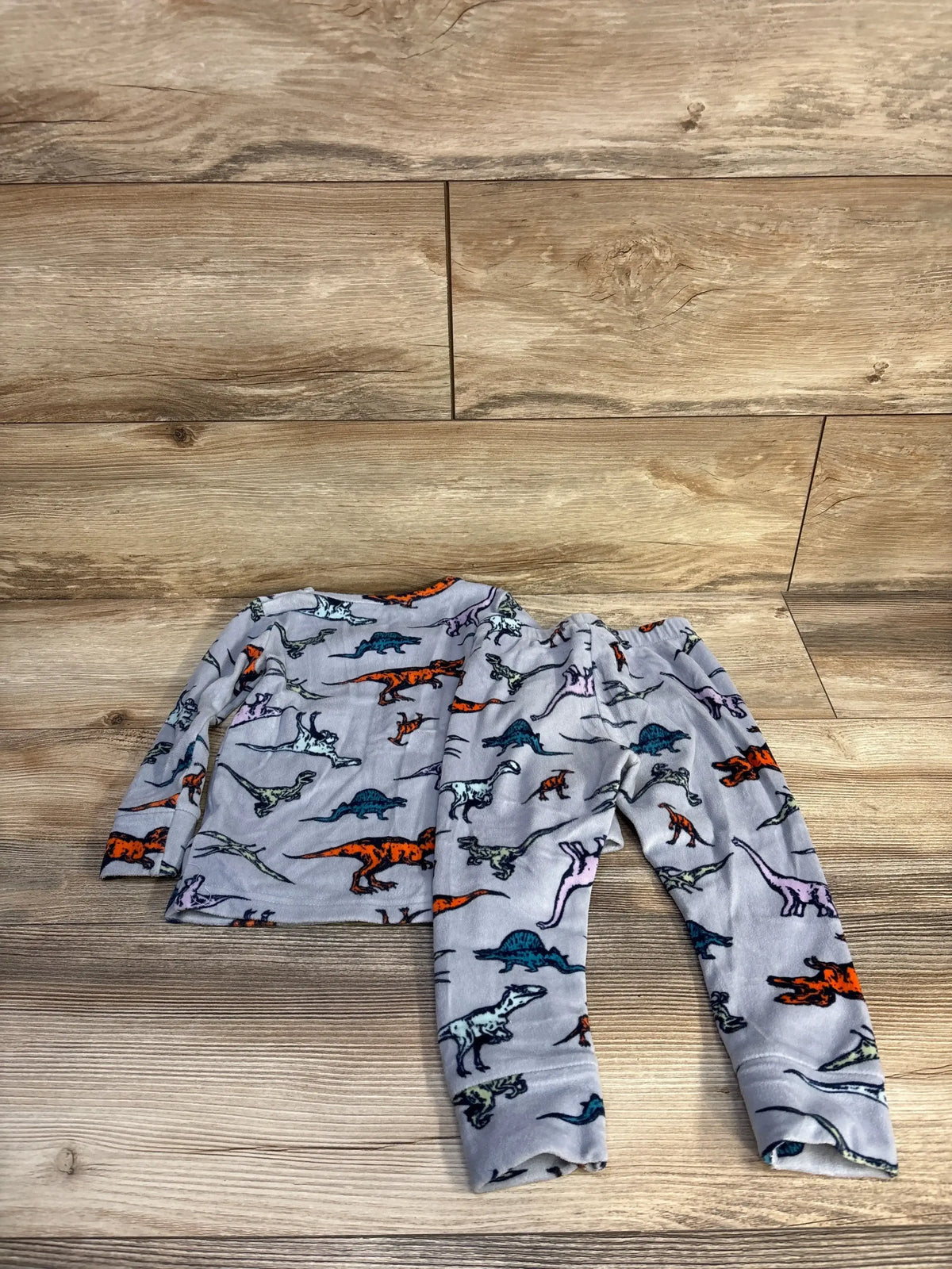 Flat lay of grey velour toddler pajama set showing multicolored dinosaur print and elastic waist on wood floor