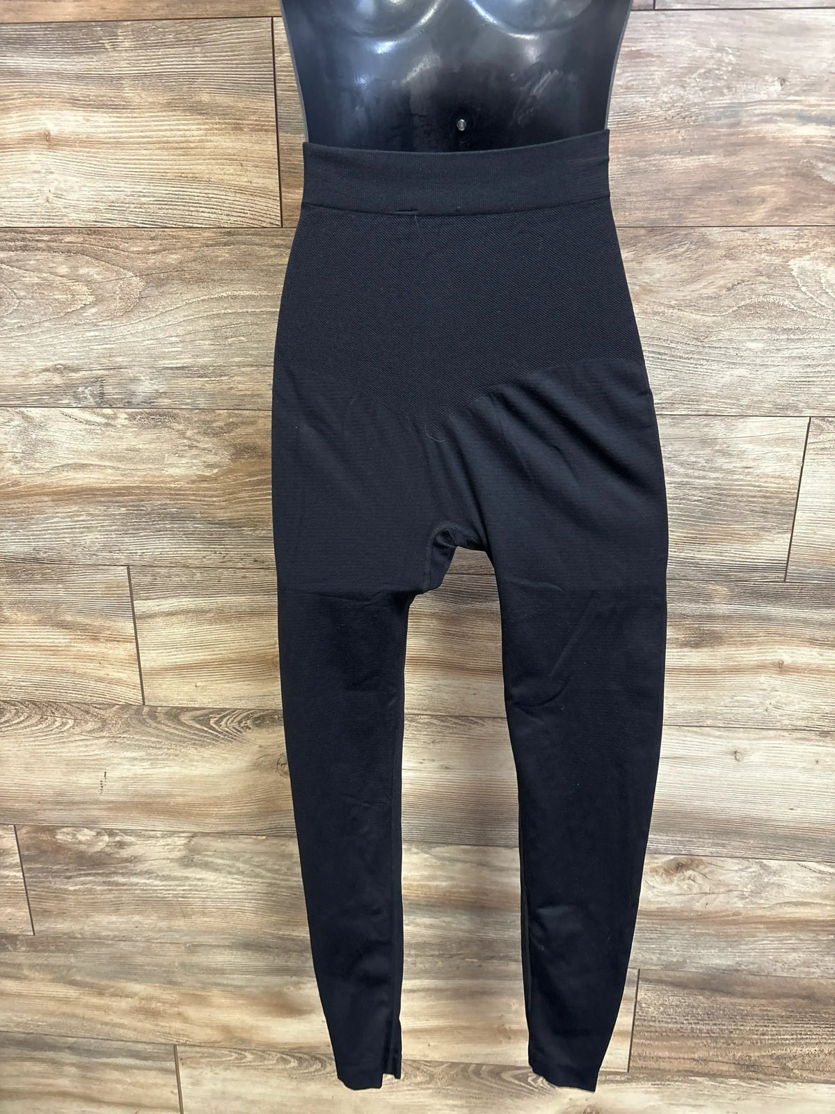 Back view of belly support maternity leggings in black showing high-rise supportive belly panel on a mannequin against wood-plank background