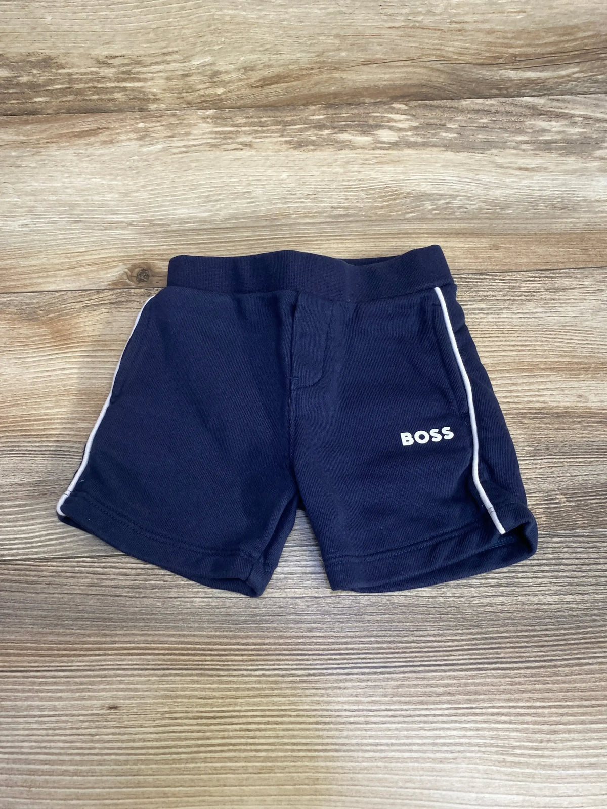 Flat lay of Boss pull on shorts in navy with white side piping and white Boss logo on wood plank floor
