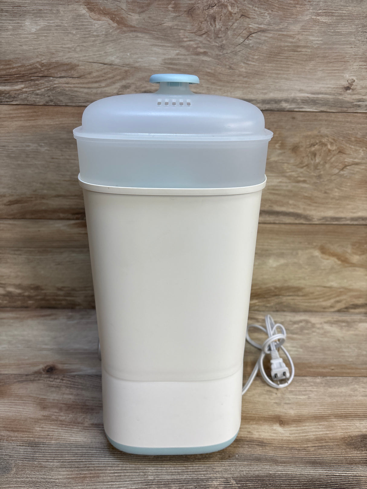 Electric baby bottle sterilizer with white base and clear lid on wood background
