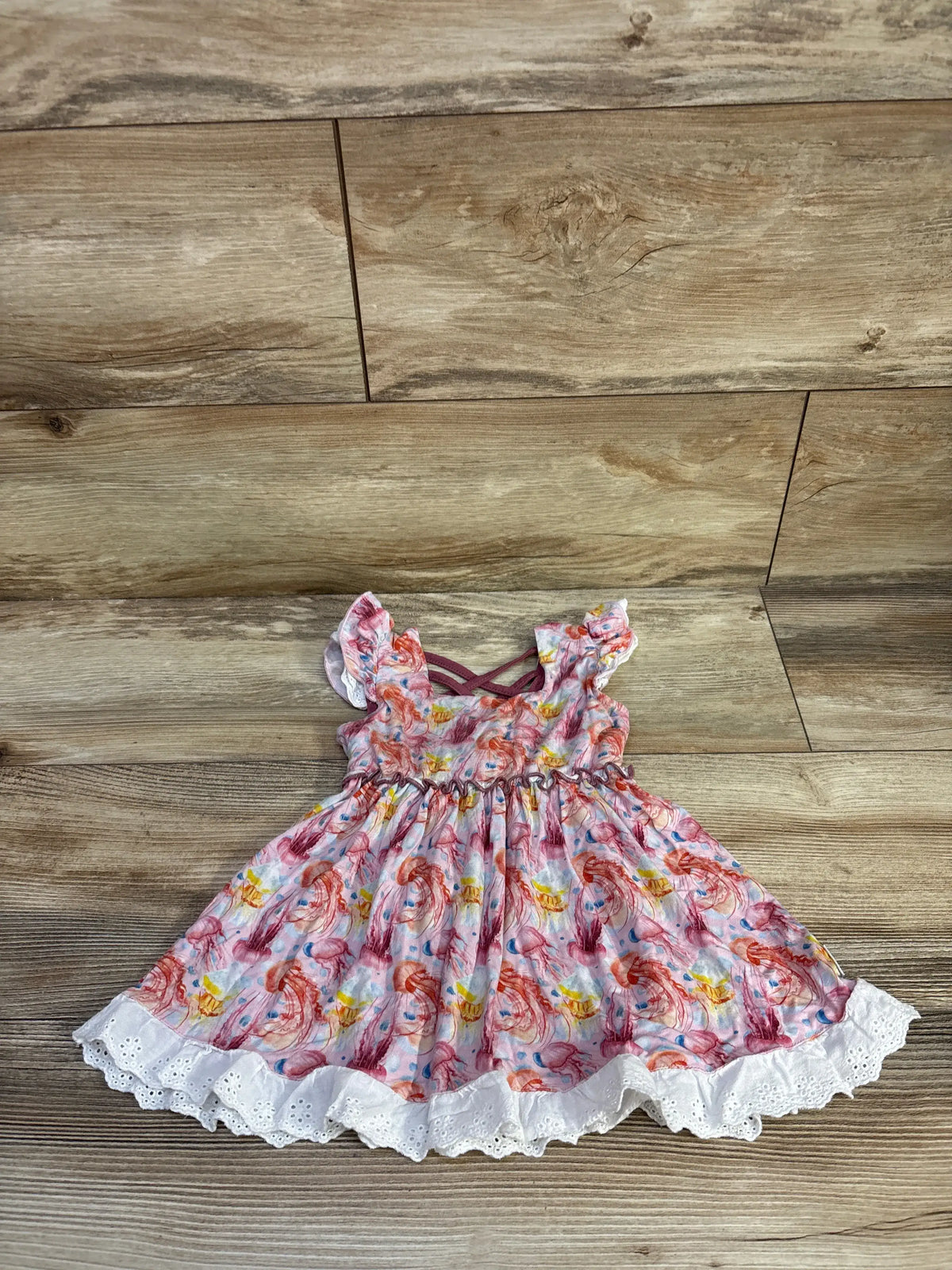 Front view of pink bamboo jellyfish dress showcasing white eyelet trim and gathered skirt on a wood floor