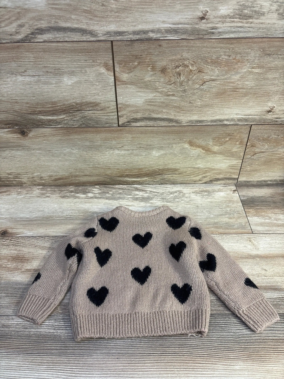 Flat lay of brown knit baby sweater with black heart print, ribbed cuffs and hem on a wood background