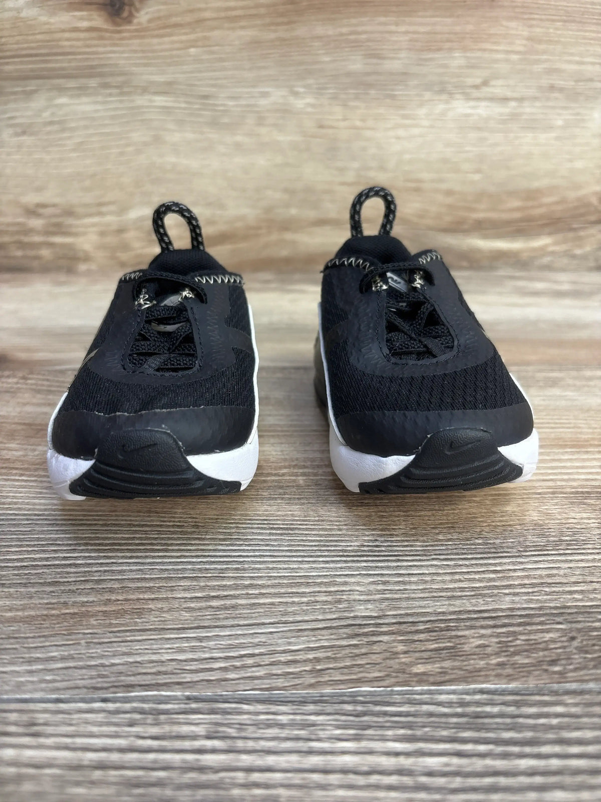 Front view of Air Max 2090 TD sneakers (sz 4C) in black showing white midsoles, elastic laces and heel pull tabs on wood background
