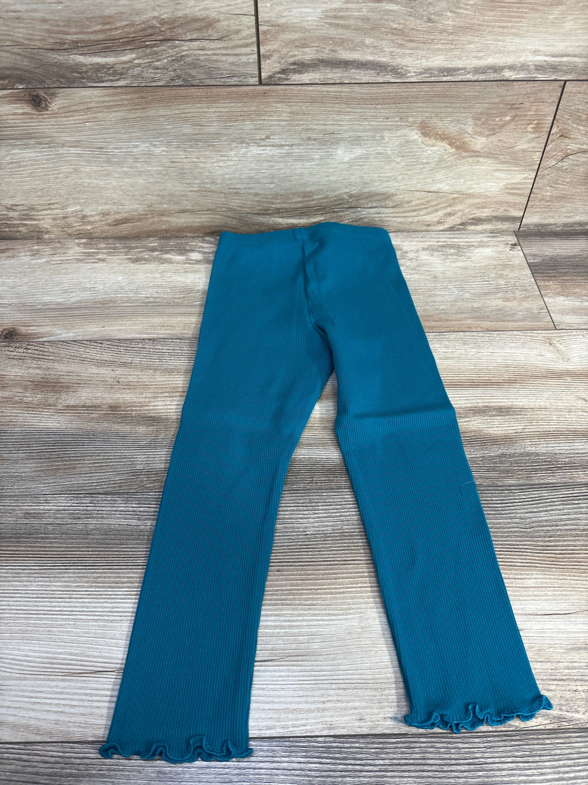 Teal ribbed toddler leggings with ruffled hems laid flat on wood floor background