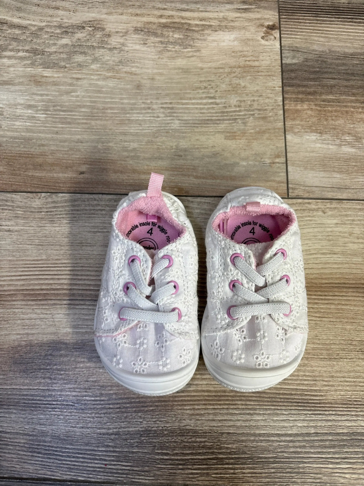 Top-down view of Wonder Nation toddler white eyelet sneakers showing pink-trimmed eyelets, laces, and removable insole marked 4C on wood floor