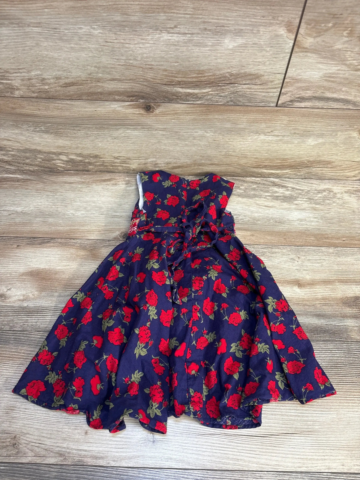 Navy blue baby dress with red rose print, sleeveless design, and tie waist, laid on wood floor