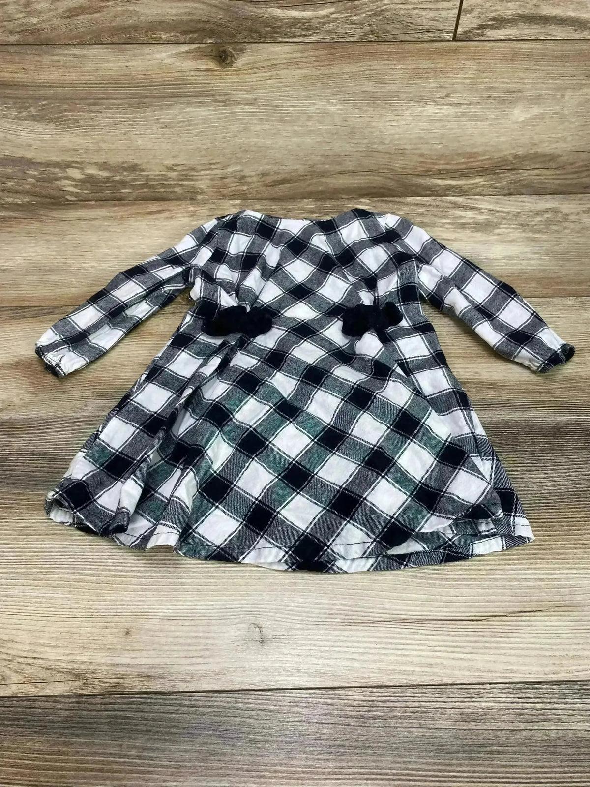 Flat lay of white and black buffalo check baby dress showcasing long sleeves and two black waist bows on a wood background