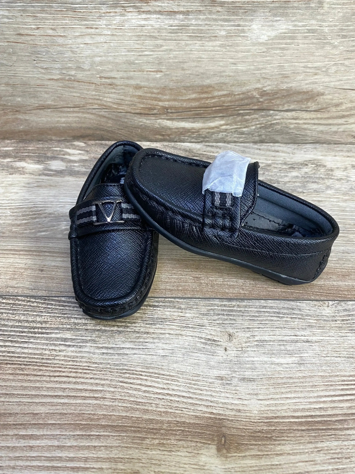 Front three-quarter view of toddler black loafers showing faux leather, metal V accent and moccasin stitching on wood
