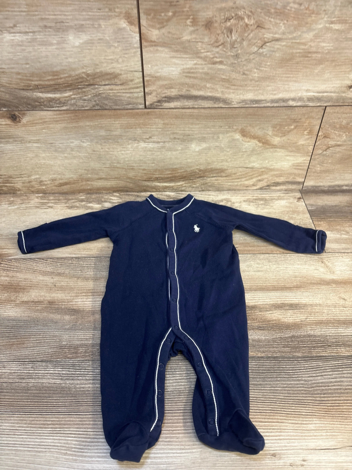 Navy blue baby footed sleeper with white trim and front snaps on wood floor