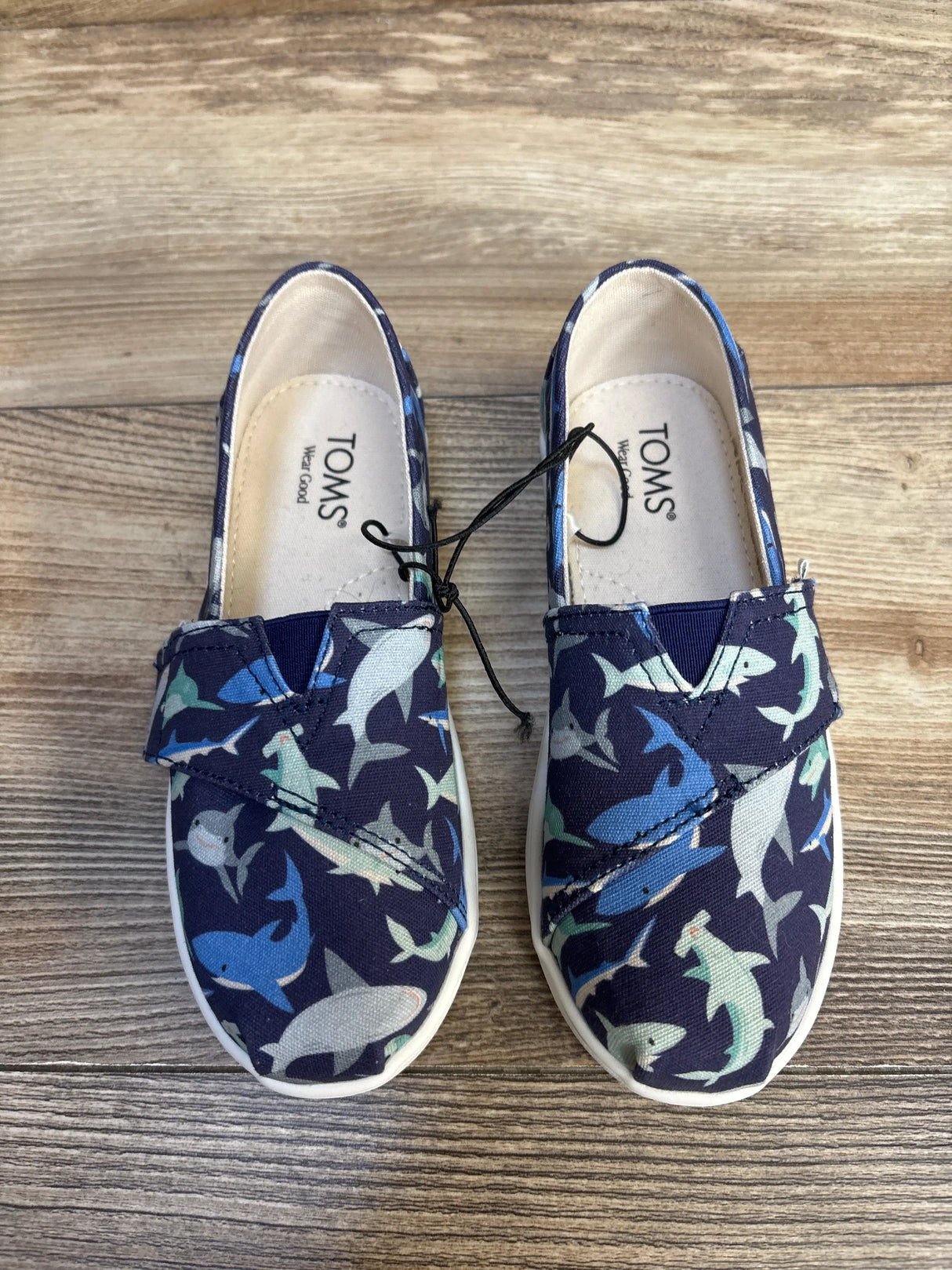 TOMS kids' slip-on shoes with shark print, navy blue canvas, white soles, on wood floor