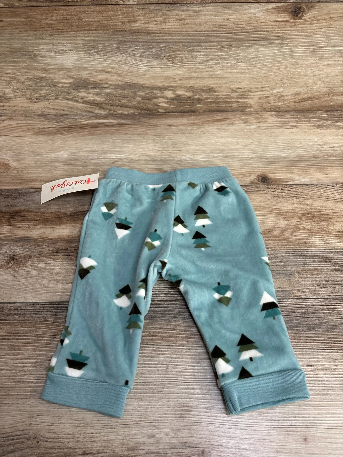Top-down view of Cat & Jack teal velour pull-on baby pants (3-6 months) showing tree print and cuffed ankles on wood background