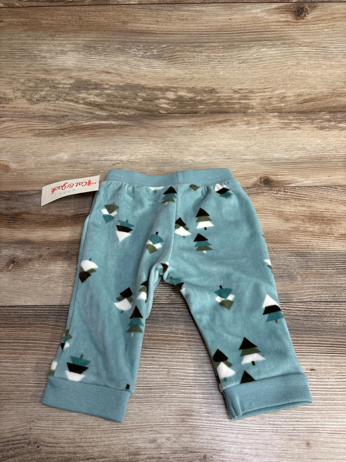 Soft blue baby pants with pine tree print, laid flat on wood background, kids clothing resale