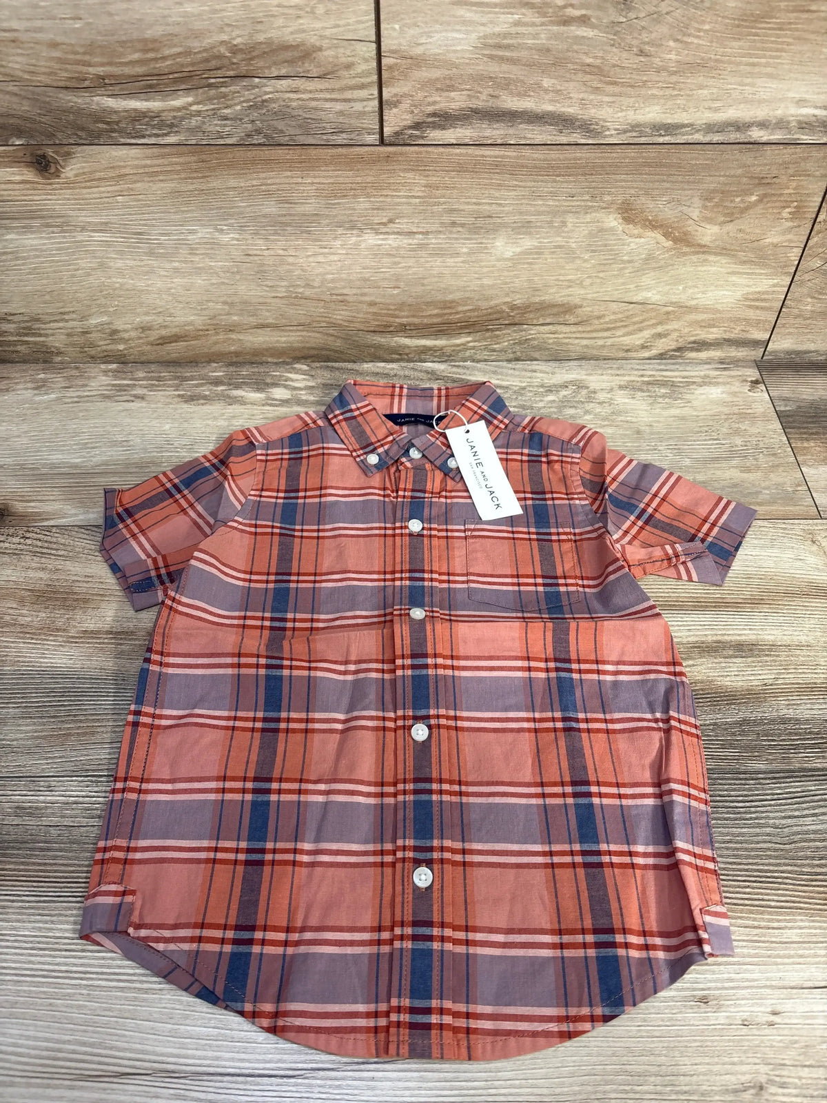 Flat lay of Janie and Jack orange and navy plaid short-sleeve button-down shirt showing front buttons and brand tag on wood, size 3T
