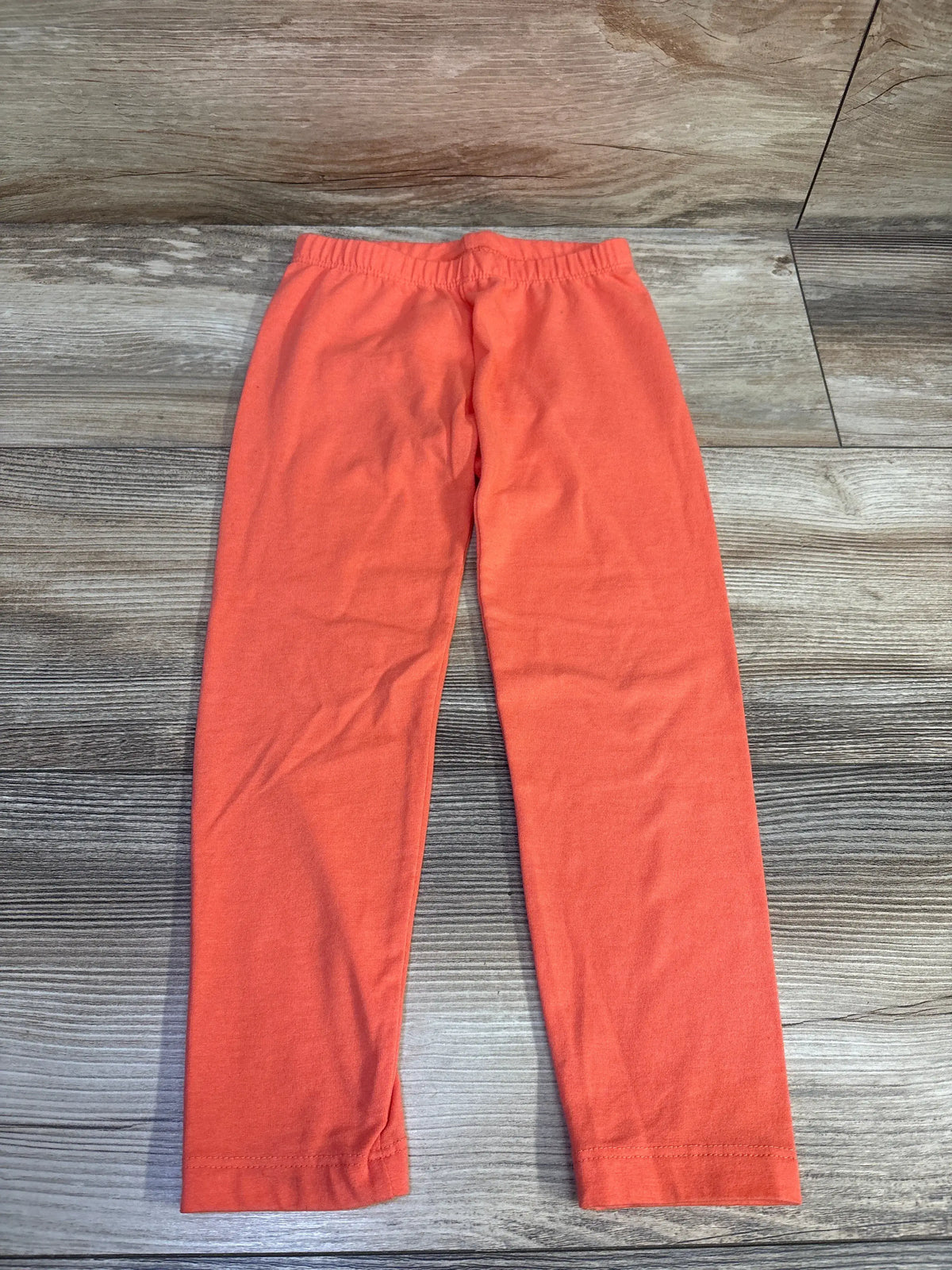 Flat lay front view of Old Navy coral toddler leggings showing elastic waistband and full-length straight legs on wood floor