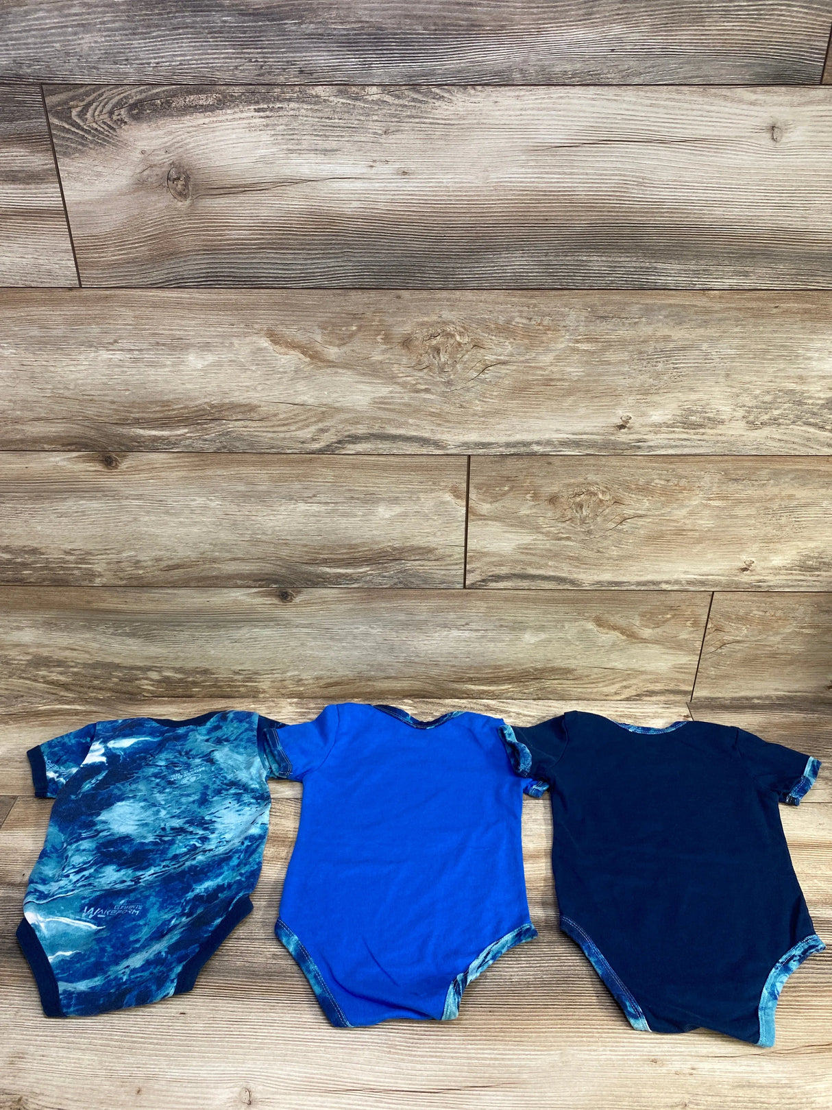 Three blue baby onesies with different patterns on a wooden background