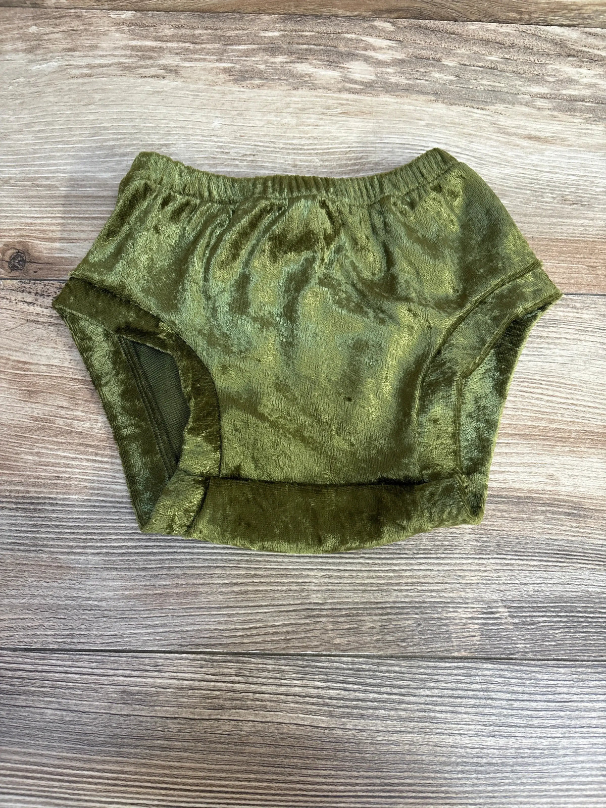 Top-down view of green velvet baby bloomers showcasing elastic waistband and plush velvet texture on light wood background