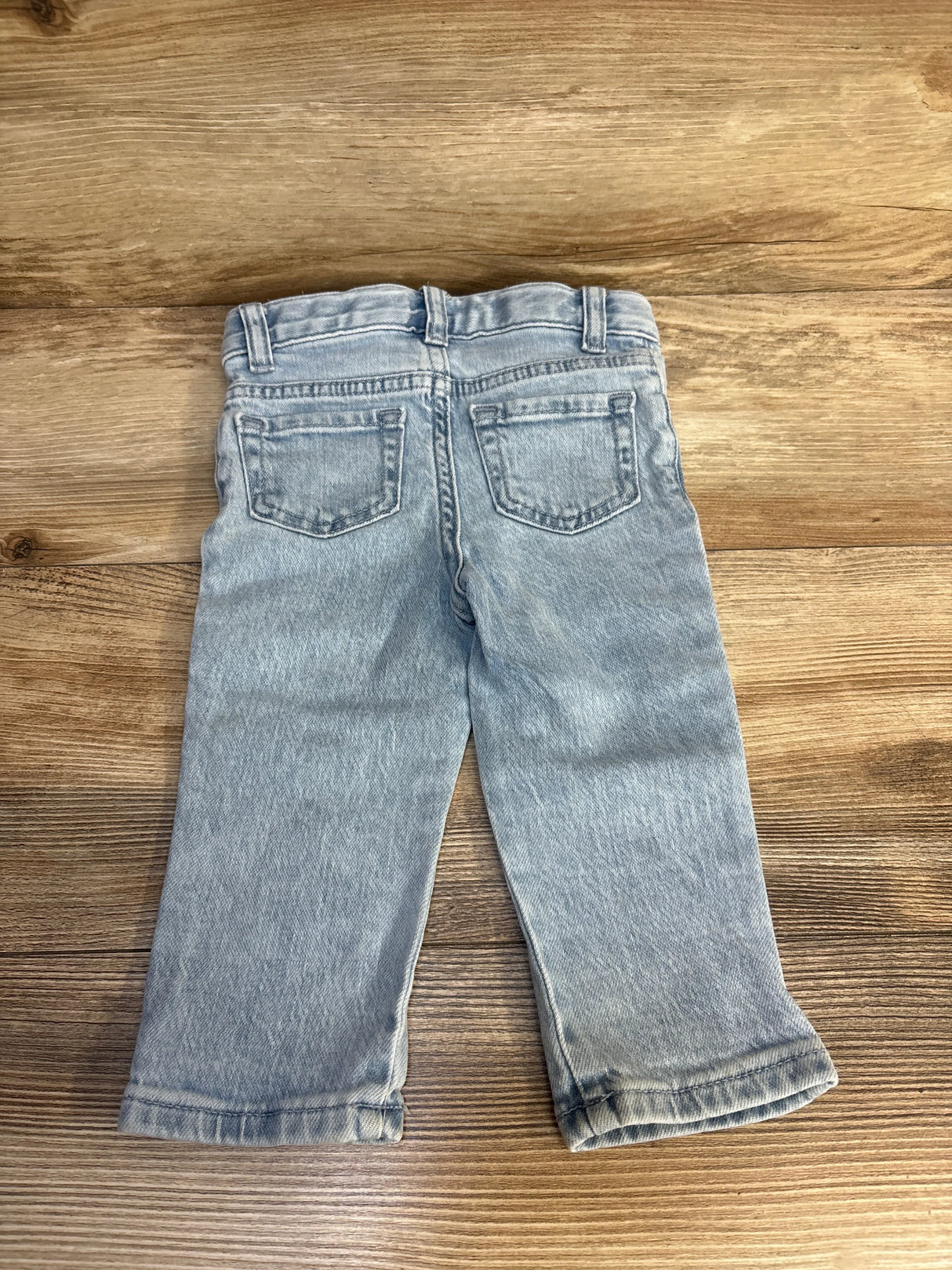 Light wash denim toddler jeans with back pockets on a wooden surface