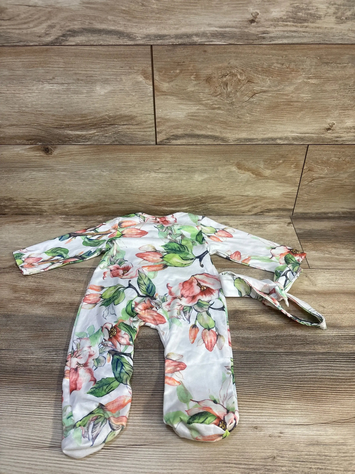 Flat lay of floral footed baby sleeper and matching headband showcasing pink and green watercolor flowers and front snap closure on wood background