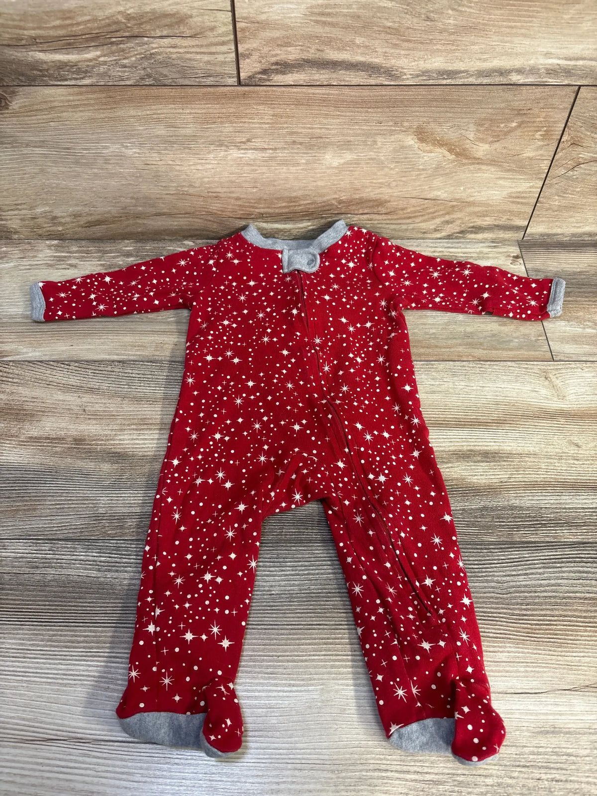 Flat lay of Honest Baby Star Sleeper showcasing red star pattern and gray trim with wood-look flooring background