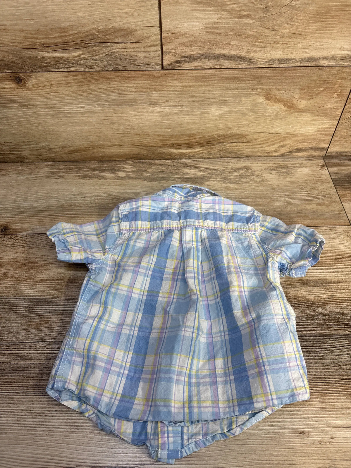 Back view of Tommy Bahama blue plaid button-up shirt in size 4T showcasing short sleeves on a wood floor