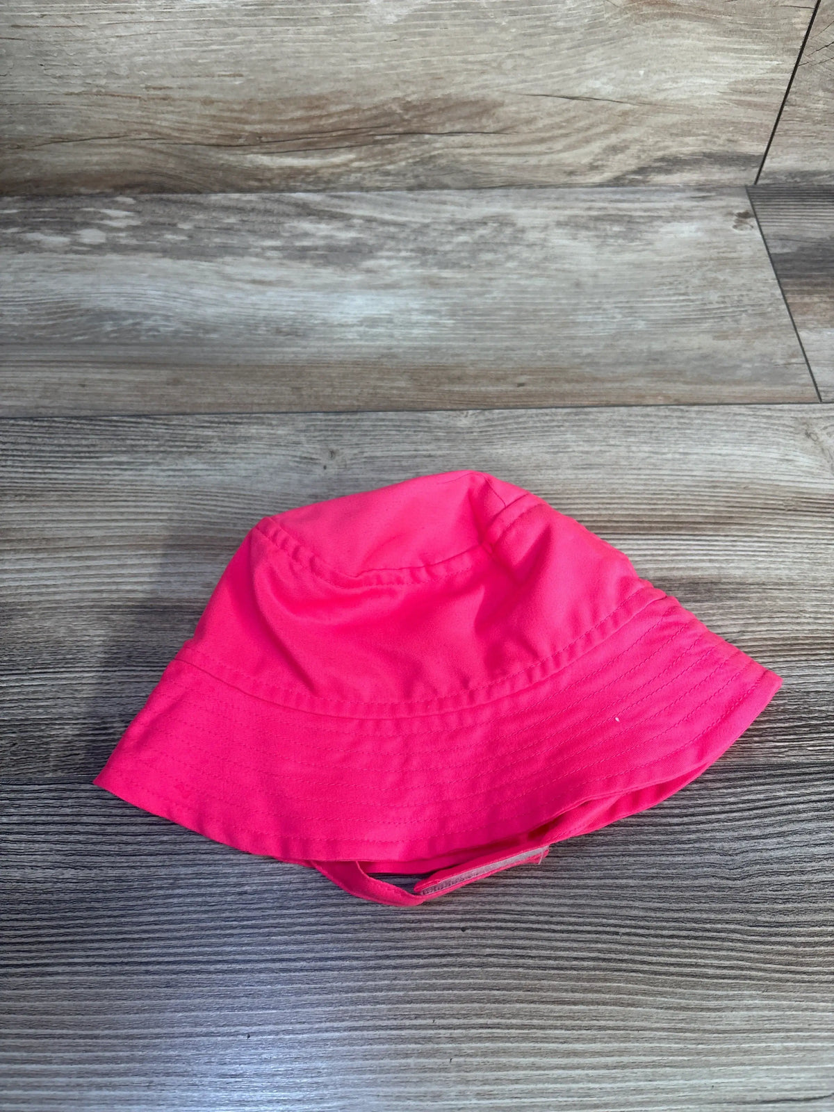 Angled view of Hurley pink bucket hat in size 18 months showcasing chin strap with Velcro closure on gray wood background
