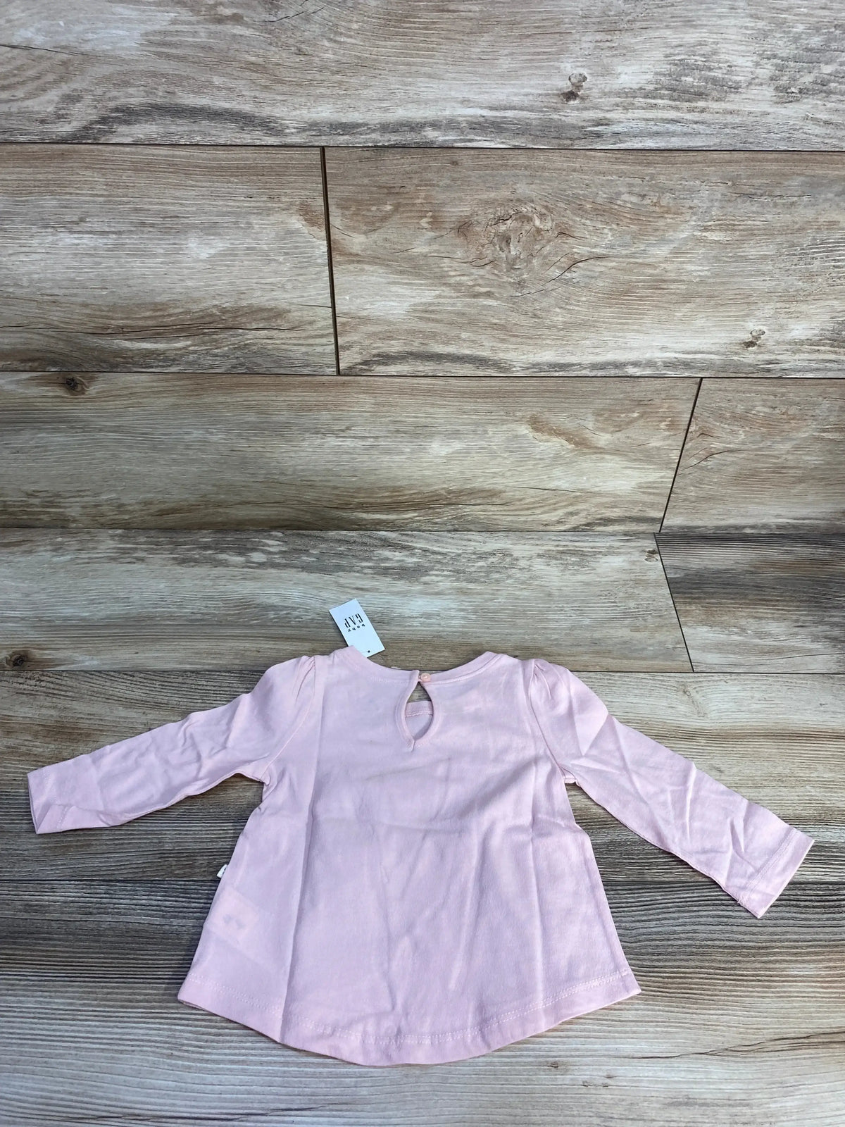 Light pink long sleeve infant shirt with tag on wood background