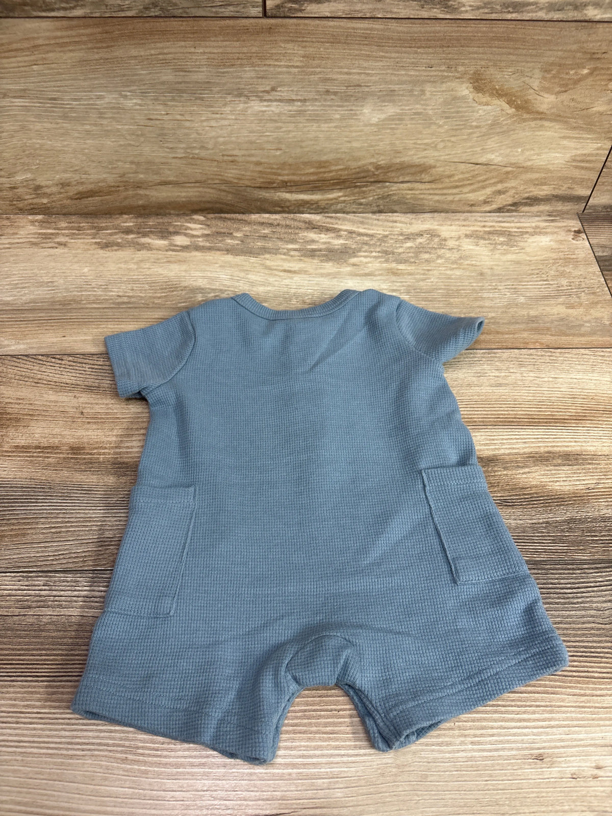 Blue Child Of Mine waffle knit henley shortie romper for infants size 0-3m on a wood background