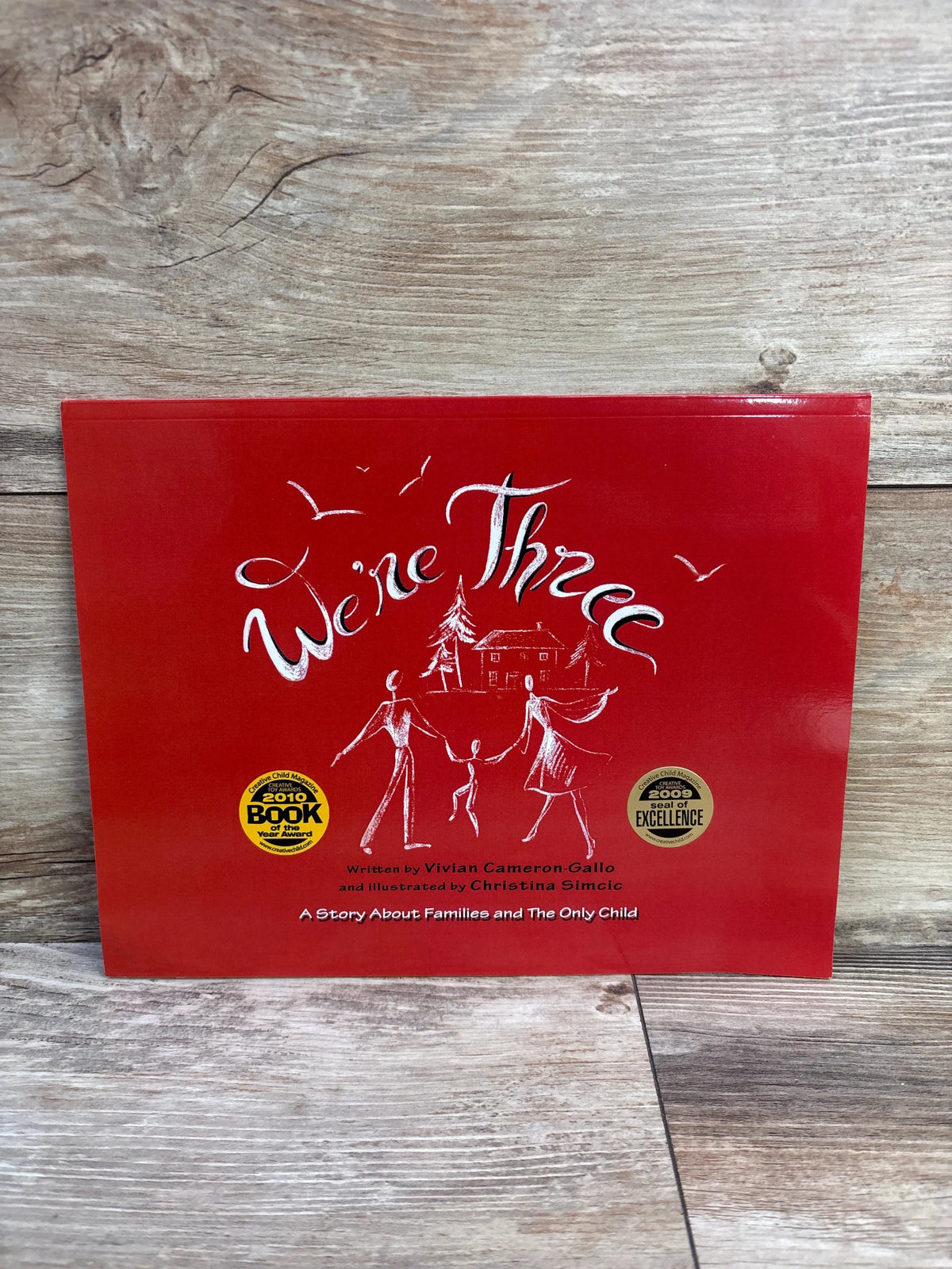 Front view of We’re Three: A Story About Families and The Only Child paperback, red cover with family illustration