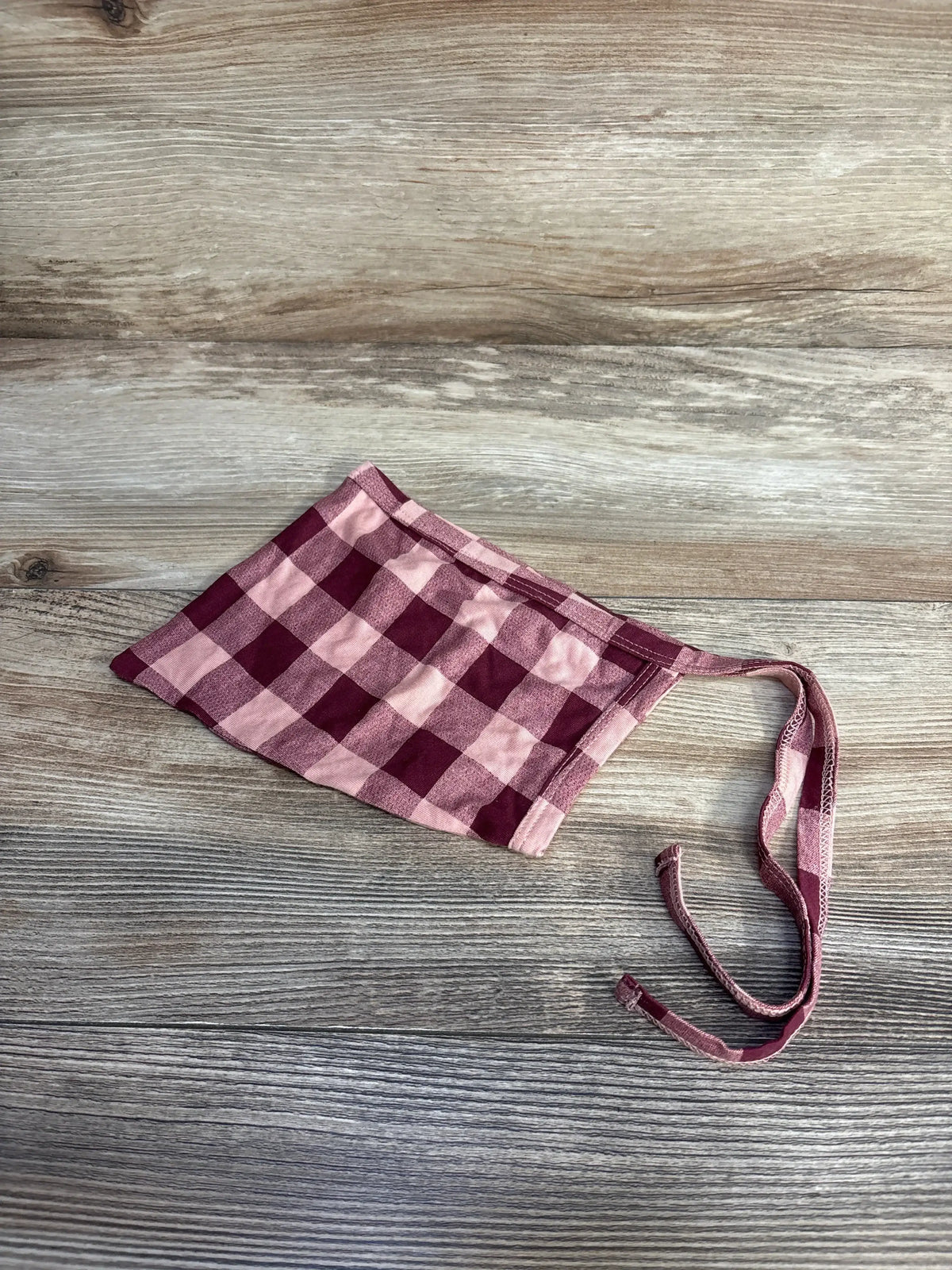 Flat lay of red and pink gingham baby bonnet size 12-18 months showing tie straps and elasticized back on wood background