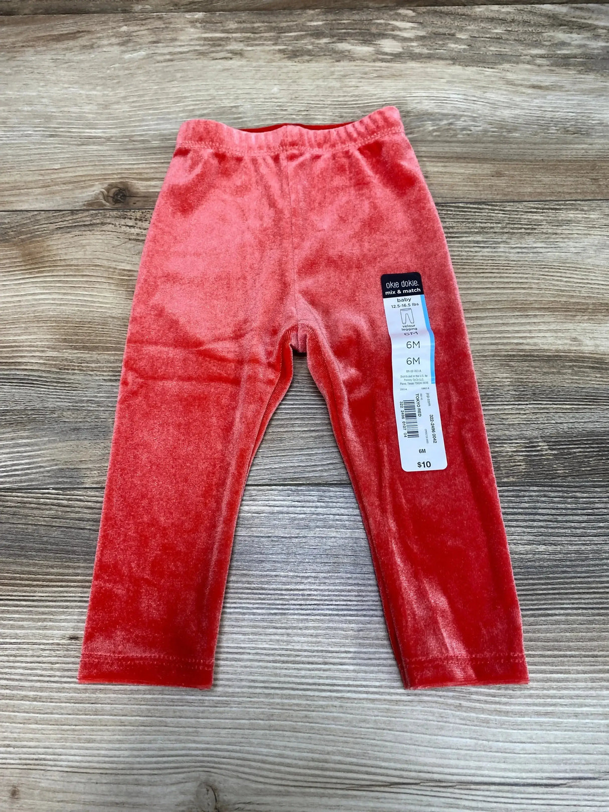 Flat lay of NEW Okie Dokie Velour Tokyo Red Leggings sz 6m showcasing coral-red velour finish elastic waistband and 6M hangtag on wood plank background
