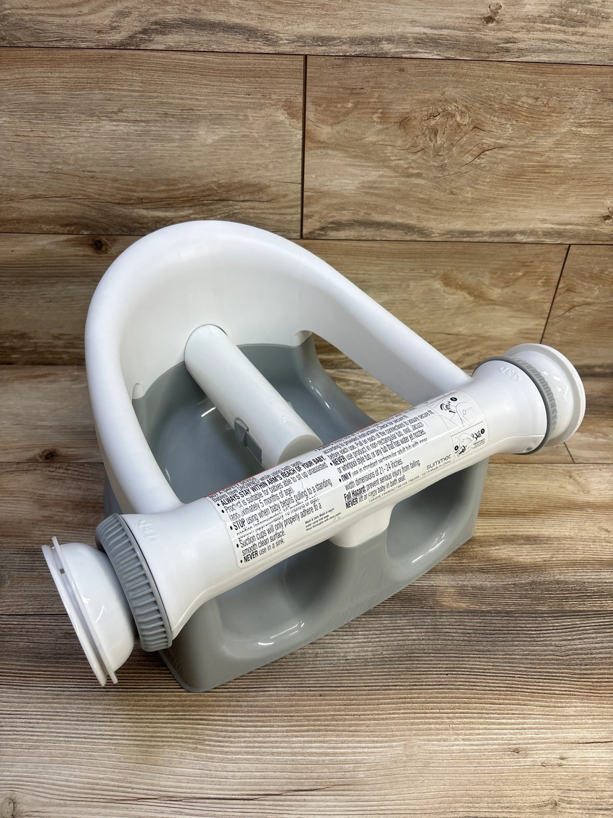 Three-quarter view of Summer Infant My Bath Seat showing white safety bar with suction cups and grey base on wood floor background
