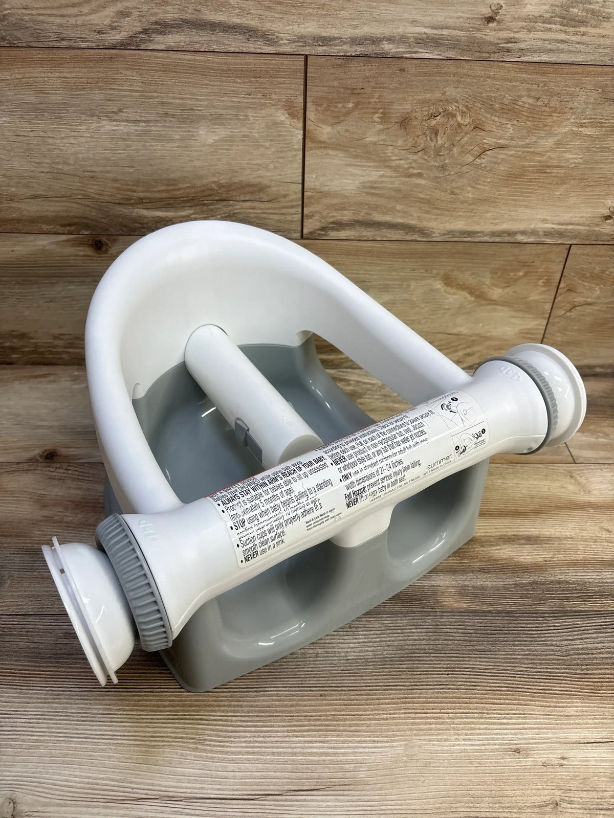 Three-quarter view of Summer Infant My Bath Seat showing white safety bar with suction cups and grey base on wood floor background