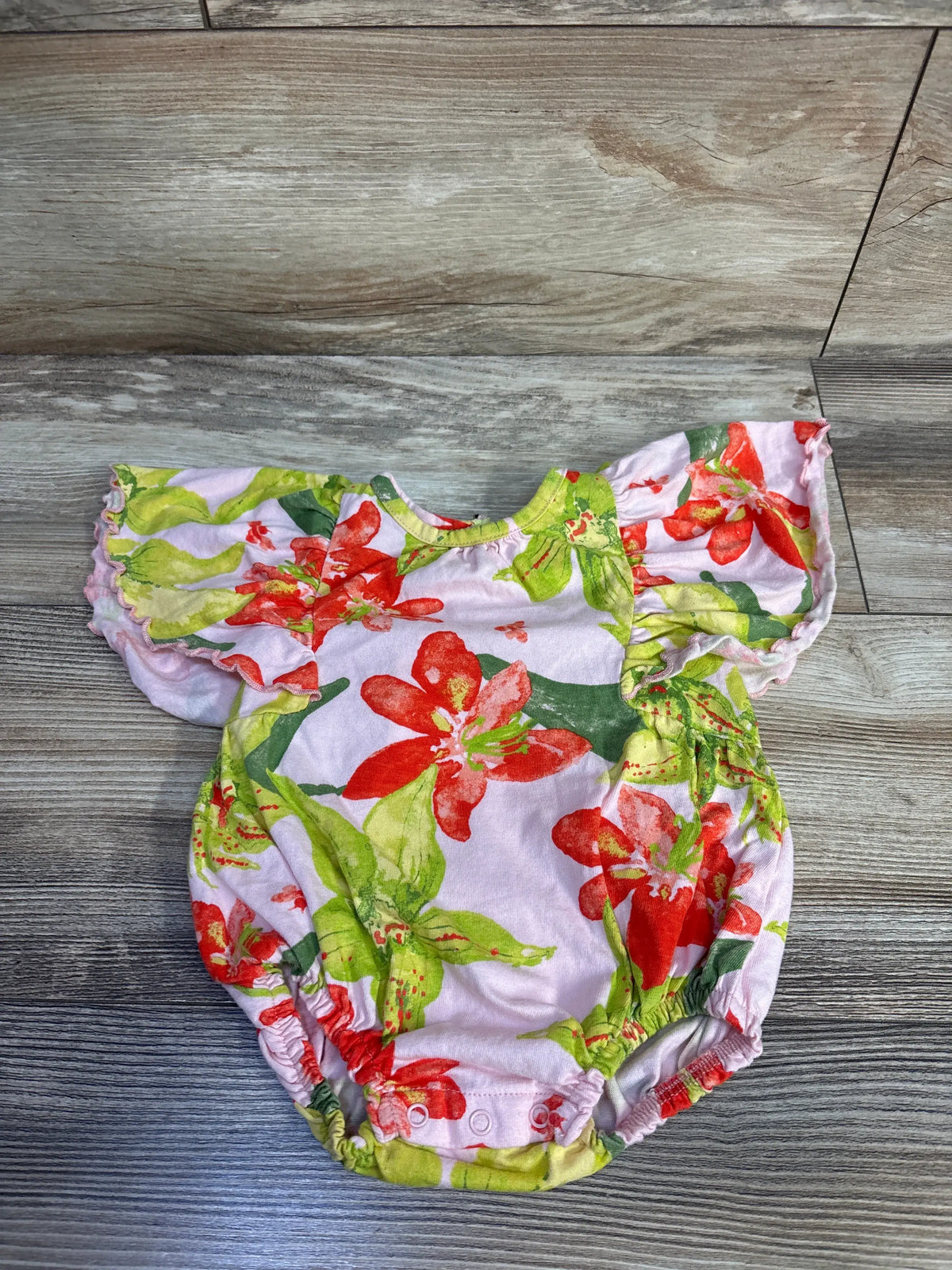 Front view of Burt’s Bees pink floral romper showcasing flutter sleeves and snap closures on wood grain