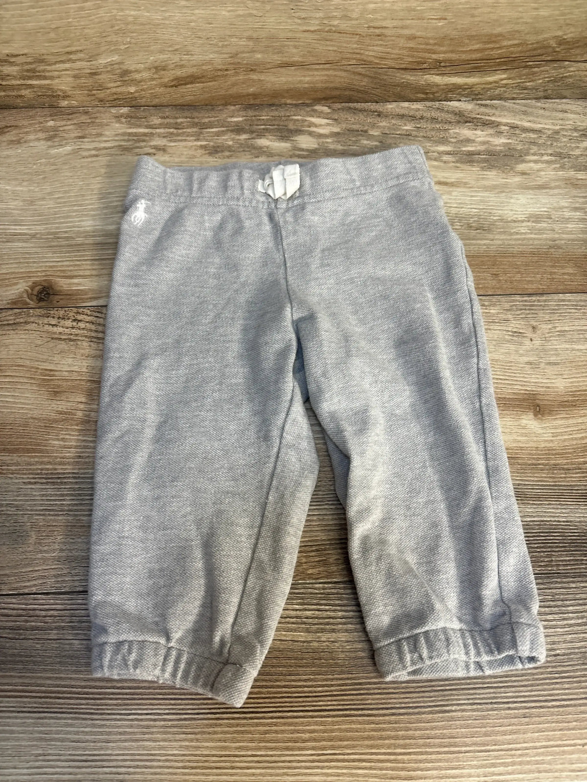 Front view of Ralph Lauren toddler drawstring pants size 12 months showcasing elastic cuffed ankles, drawstring waistband, and small embroidered pony on wooden background