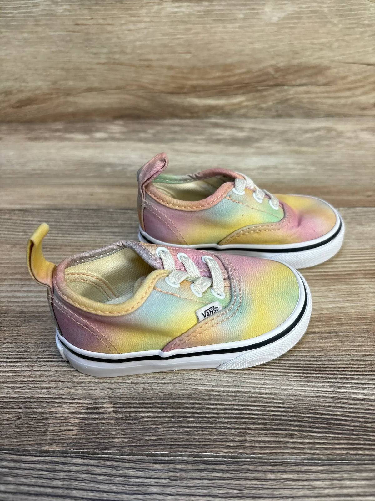 Toddler tie-dye Vans sneakers with pastel rainbow colors on wooden background