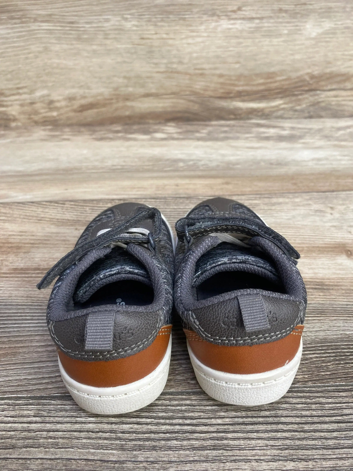 Rear view of Carter's Gustav casual toddler sneakers in gray size 6C, showing brown heel panels, Velcro straps, and white rubber soles on wooden floor