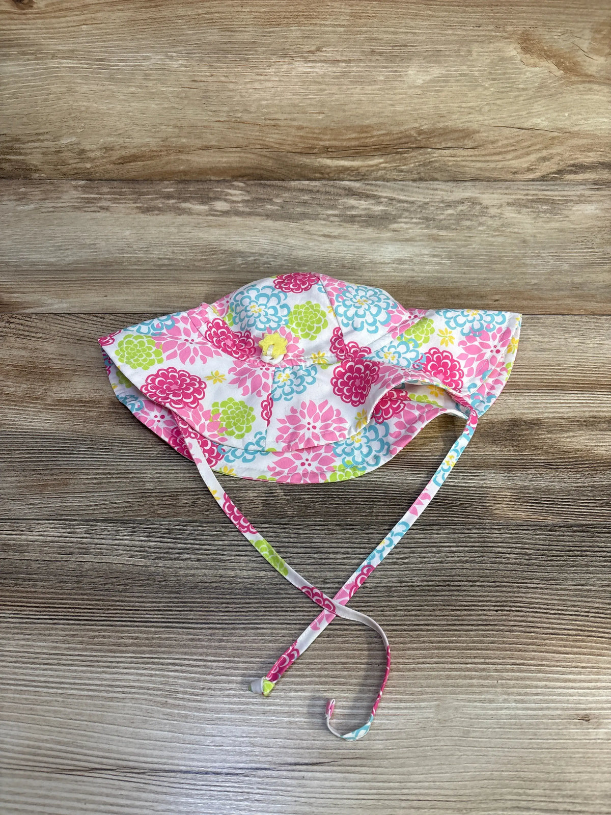 Top view of iPlay by Green Sprouts white swim bucket hat showcasing colorful floral pattern and chin strap on a wood surface