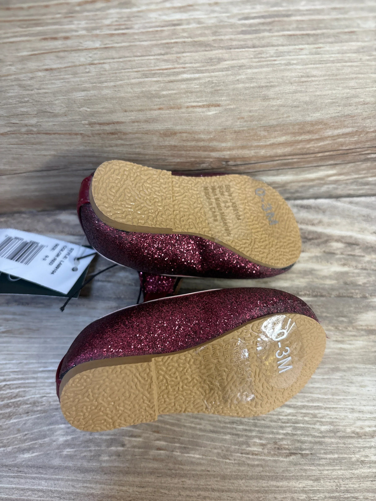 Bottom view of Laura Ashley maroon sparkly Mary Jane baby flats with textured tan soles and 0 to 3 month marking on wood