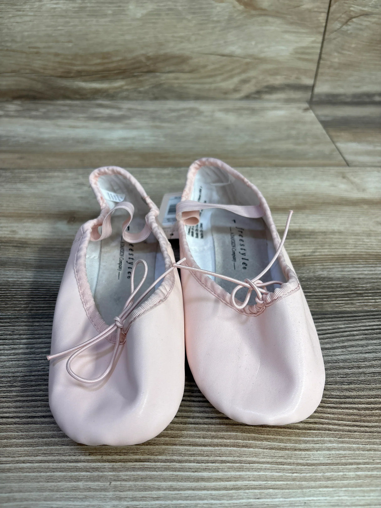 Pair of pink ballet shoes with bows on wooden floor