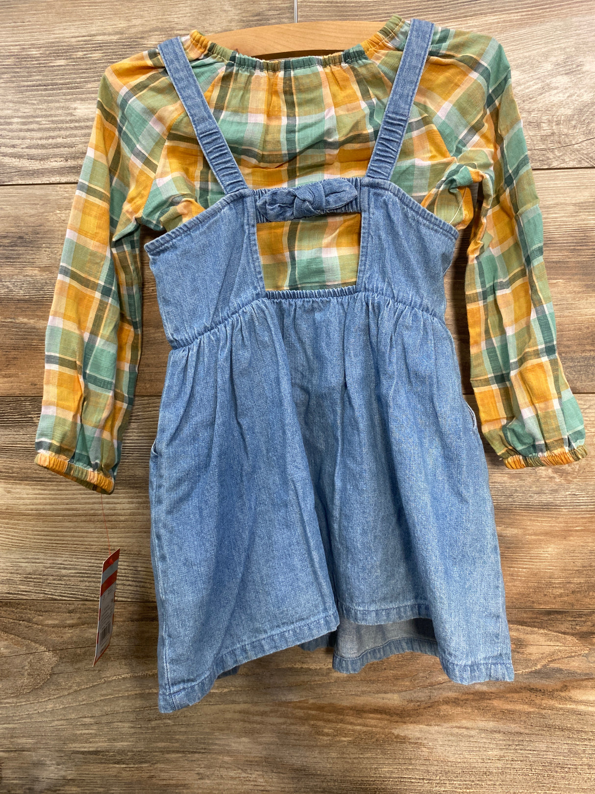 Child's outfit with plaid long-sleeve shirt in orange and green and denim dress with straps on wood background