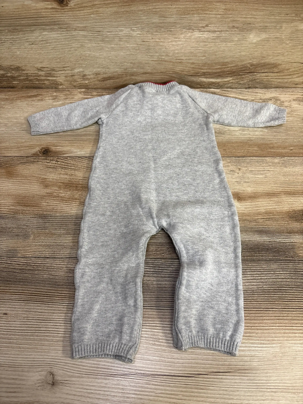 Gray knit baby onesie with red trim, laid flat on wood floor for kids clothing resale