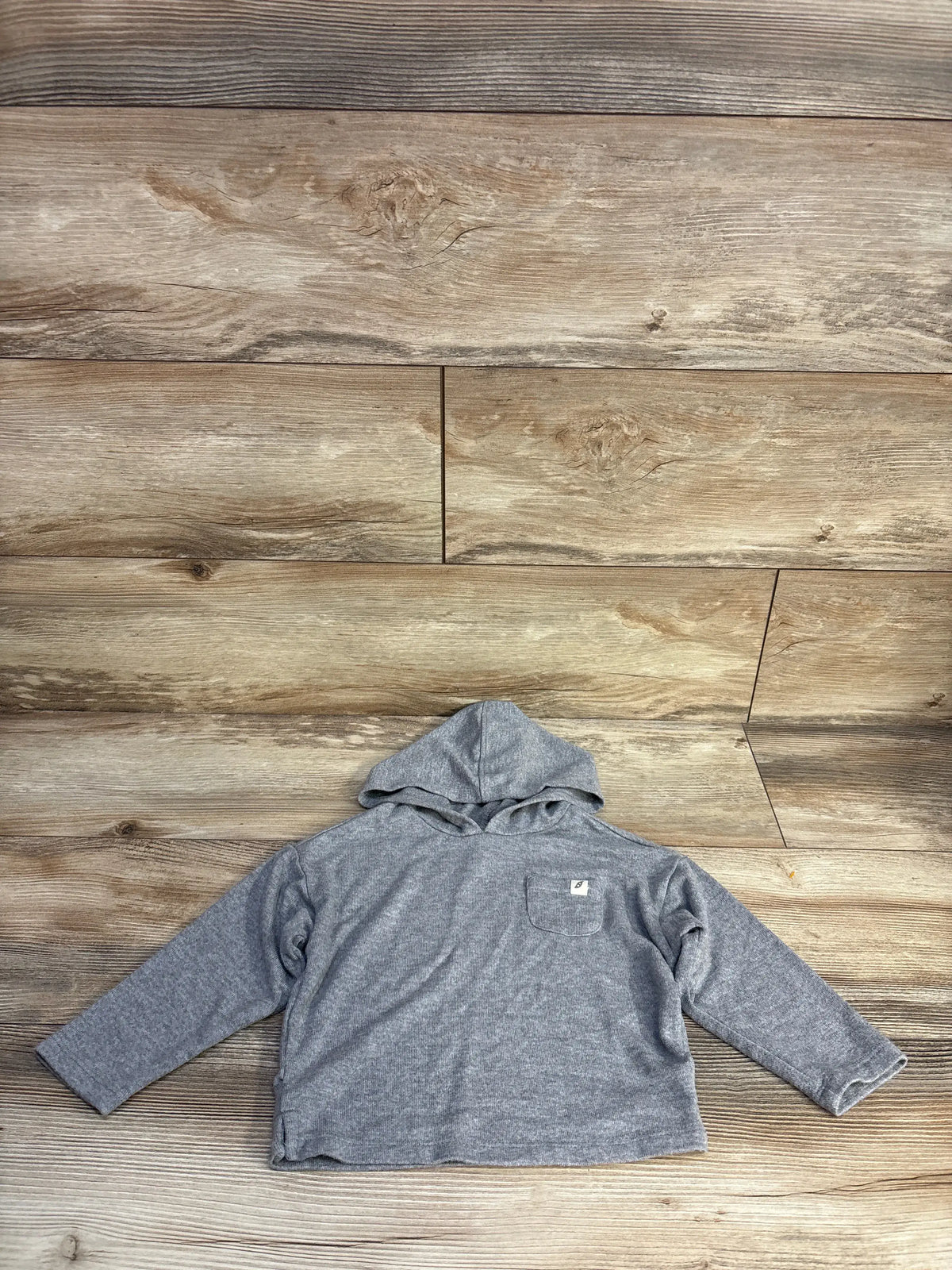 Front view of Easy Peasy grey hooded shirt with long sleeves and chest pocket on a wood-grain background